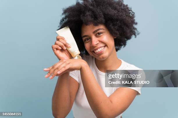 afro style young woman applying moisturizing cream on her hands while smiling and looking at the camera isolated. - bothies stock pictures, royalty-free photos & images