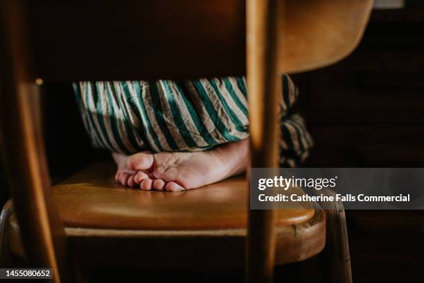 a child sits on their feet on a chair - kids feet in home stock pictures, royalty-free photos & images