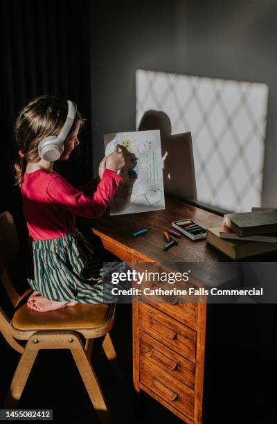 a little girl wearing wireless headphones proudly shows off her sketch - ear plug ear protectors stock pictures, royalty-free photos & images