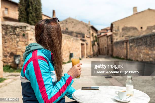 young blonde woman drinking juice on a terrace of a bar in an old spanish town. - ロマネスク ストックフォトと画像