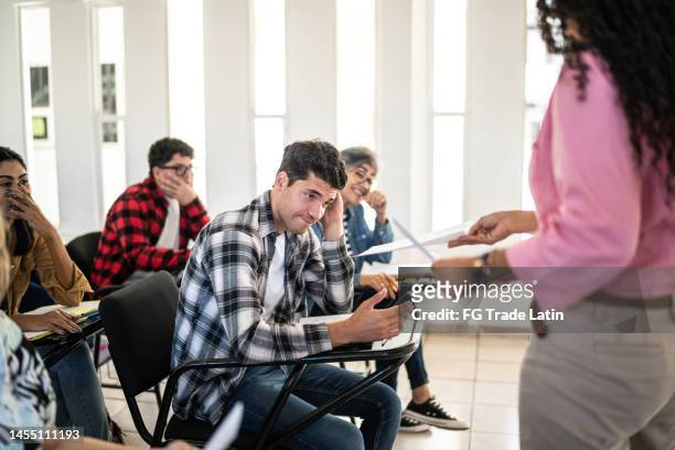 young man receiving his test result in the classroom at university - test results stock pictures, royalty-free photos & images
