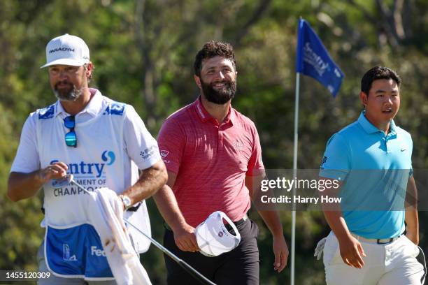 Jon Rahm of Spain smiles after making his putt for birdie on the 18th green as he walks off alongside caddie Adam Hayes and Tom Kim of South Korea...
