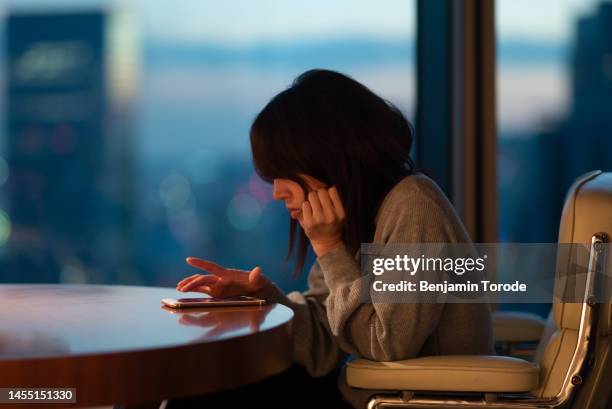 japanese woman sitting at desk operating smartphone with fingers - bad posture fotografías e imágenes de stock