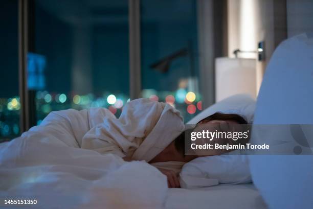 japanese woman asleep in bed with city lights in background - ベッド ストックフォトと画像