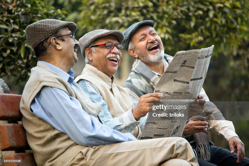 Older male friends reading newspaper at park