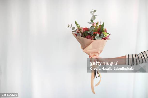 bouquet of eucalyptus twigs and flowers in craft paper in hand of florist on white background. - bouquet stock-fotos und bilder
