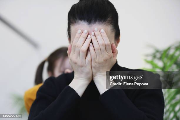 tired mother sitting at the cafe, covering face by hands and her playful daughter playing around - woman head in hands sad stock pictures, royalty-free photos & images