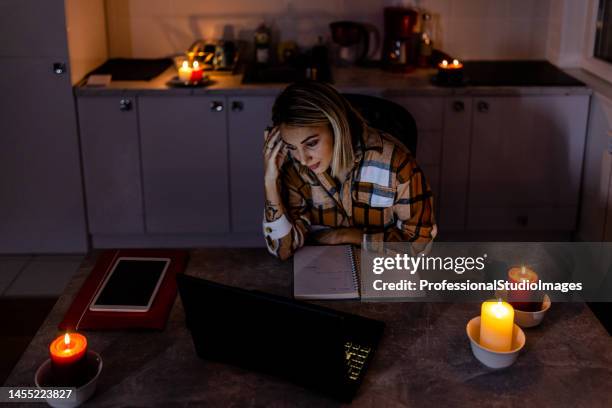 a woman is working on a laptop in a dark room caused by an electric crisis and a blackout. - kaarslicht stockfoto's en -beelden