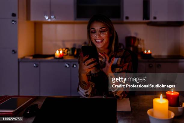 während einer energetischen krise arbeitet eine frau an einem laptop mit einem handy im dunkeln mit brennenden kerzen. - blackout stock-fotos und bilder