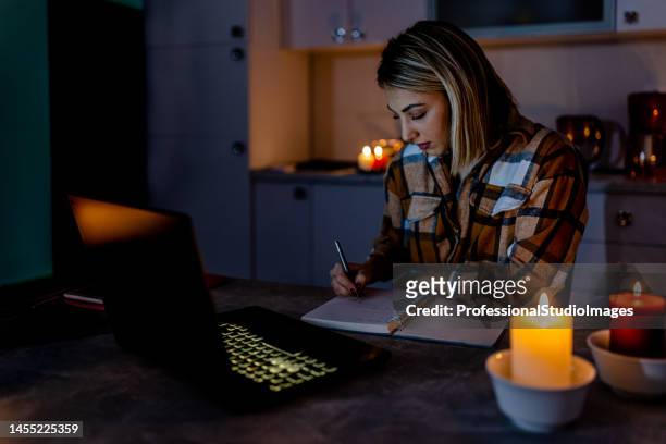 durante una crisi energetica, una donna lavora a casa al buio con candele accese. - candle light foto e immagini stock