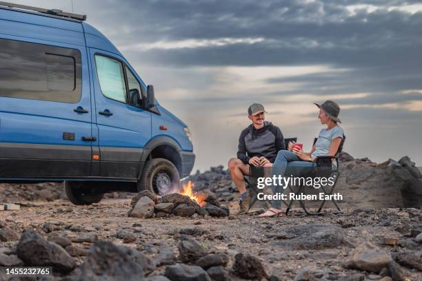 young couple drinking coffee in front of a bonfire while wild camping with their camper van, lanzarote - wanderer stock pictures, royalty-free photos & images