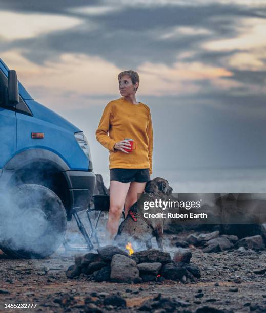 female traveler with her dog drinking coffee next to a camper van and a bonfire, lanzarote - short haired dogs stock pictures, royalty-free photos & images