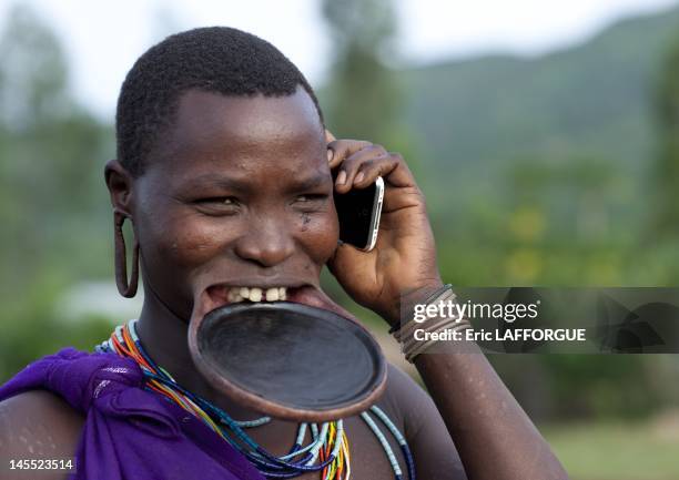 Suri woman with lip plate and mobile phone on July 5, 2010 in Turgit village, Omo Valley, Ethiopia. Piercing and lip plates are a strong part of the...