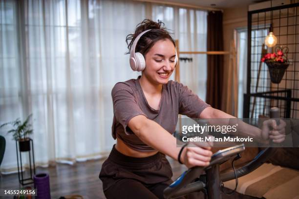 a young fitness woman rides an exercise bike in the living room - open workouts imagens e fotografias de stock