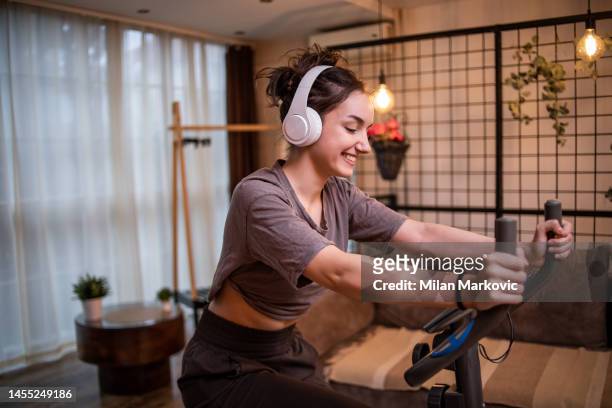 a young fitness woman rides an exercise bike in the living room - open workouts imagens e fotografias de stock