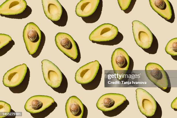 pattern of fresh ripe green avocado fruit halves on beige background. healthy food, diet and detox concept. flat lay, top view - guacamole stock-fotos und bilder