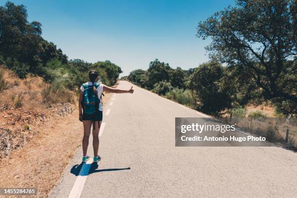 blonde girl with braid and green backpack doing hitchhiking in monfrague national park - trampen stock-fotos und bilder
