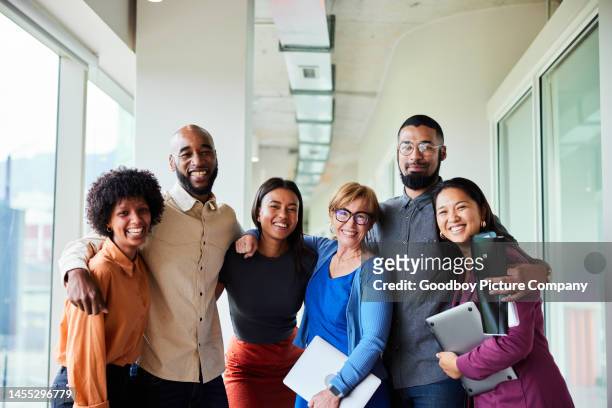 empresarios sonrientes tomados del brazo en un pasillo de oficinas - grupo multiétnico fotografías e imágenes de stock