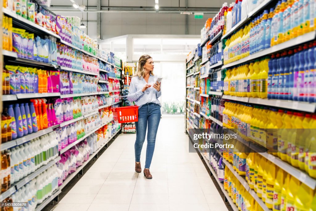Woman customer with mobile phone buying groceries in store