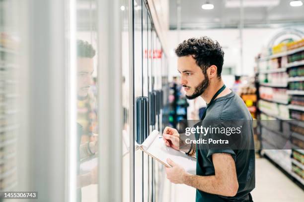 salesman updating stock of groceries at supermarket - corner shop stock pictures, royalty-free photos & images