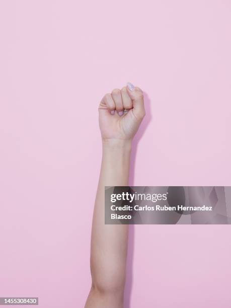 woman's raised fist in protest form on a pink background. - puño en alto fotografías e imágenes de stock