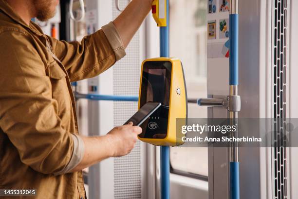 contactless payment. young man processing payment while on public transportation. man paying with mobile phone for a ride on a tram. male buying ticket via digital wallet. close up - fare fotografías e imágenes de stock