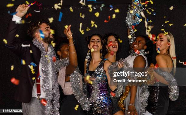 fröhliche gruppe von freunden tanzt während eines neujahrs-countdowns, während buntes konfetti herunterfällt - black balloon stock-fotos und bilder