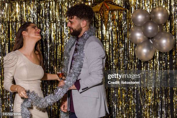 girlfriends dancing and playing with silver tinsel garland when celebrating new year's eve - photo booth couple stock pictures, royalty-free photos & images