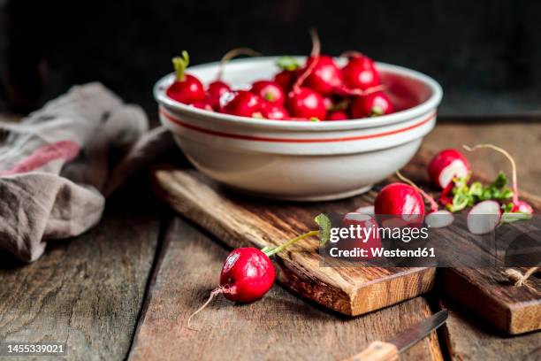 fresh radishes in bowl on cutting board at table - radish stockfoto's en -beelden