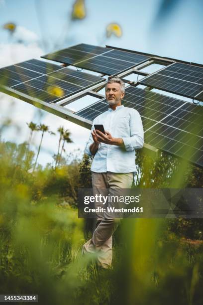 mature man leaning on solar panels with smart phone at garden - solar panel array front view stock pictures, royalty-free photos & images