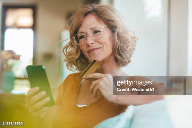 smiling mature woman with credit card using smart phone at home - banking stock pictures, royalty-free photos & images