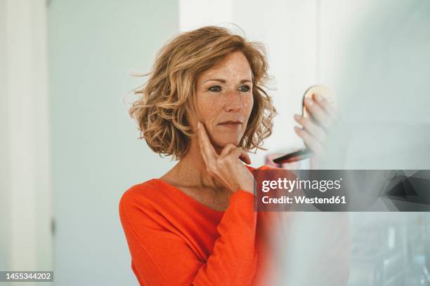 smiling mature woman looking in mirror at home - spiegel stock-fotos und bilder