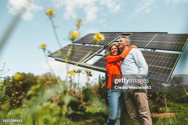 mature woman hugging man standing in front of solar panels - self sufficiency fotografías e imágenes de stock