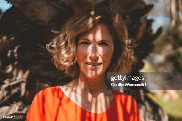 smiling blond woman standing in front of tree - 50 sombras fotografías e imágenes de stock