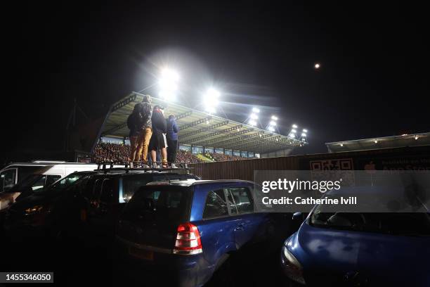 Fans watch match action from outside the stadium whilst standing on a car during the Emirates FA Cup Third Round match between Oxford United and...