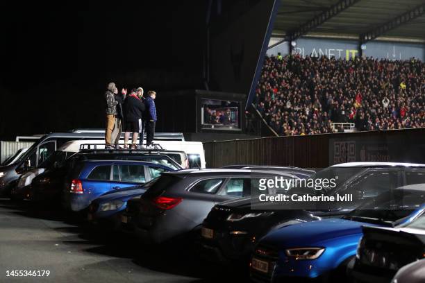 Fans watch match action from outside the stadium whilst standing on a car during the Emirates FA Cup Third Round match between Oxford United and...