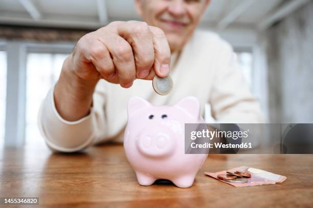 man putting coin into piggy bank at home - spaarpot financieel item stockfoto's en -beelden