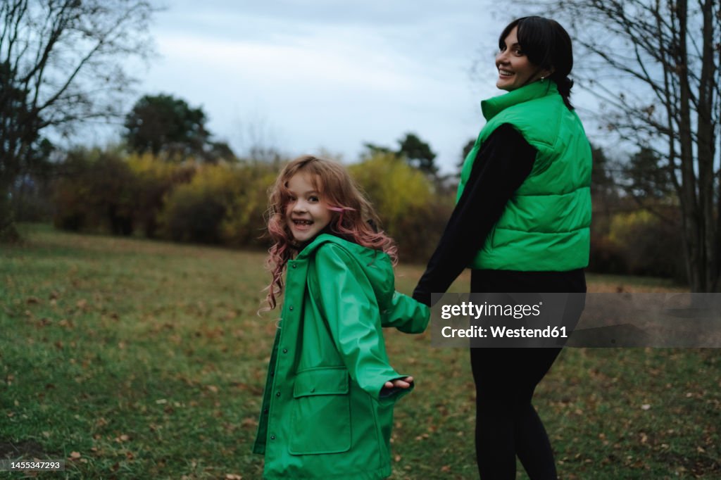 Happy girl holding hands with mother walking in park