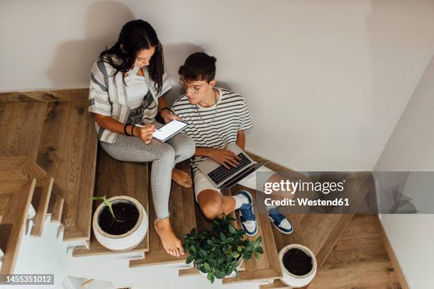 sibling studying together through tablet pc sitting on staircase at home - liens relationels photos et images de collection