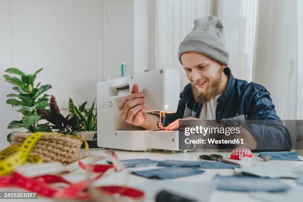 smiling fashion designer working on sewing machine in workshop - sewing machine stock-fotos und bilder