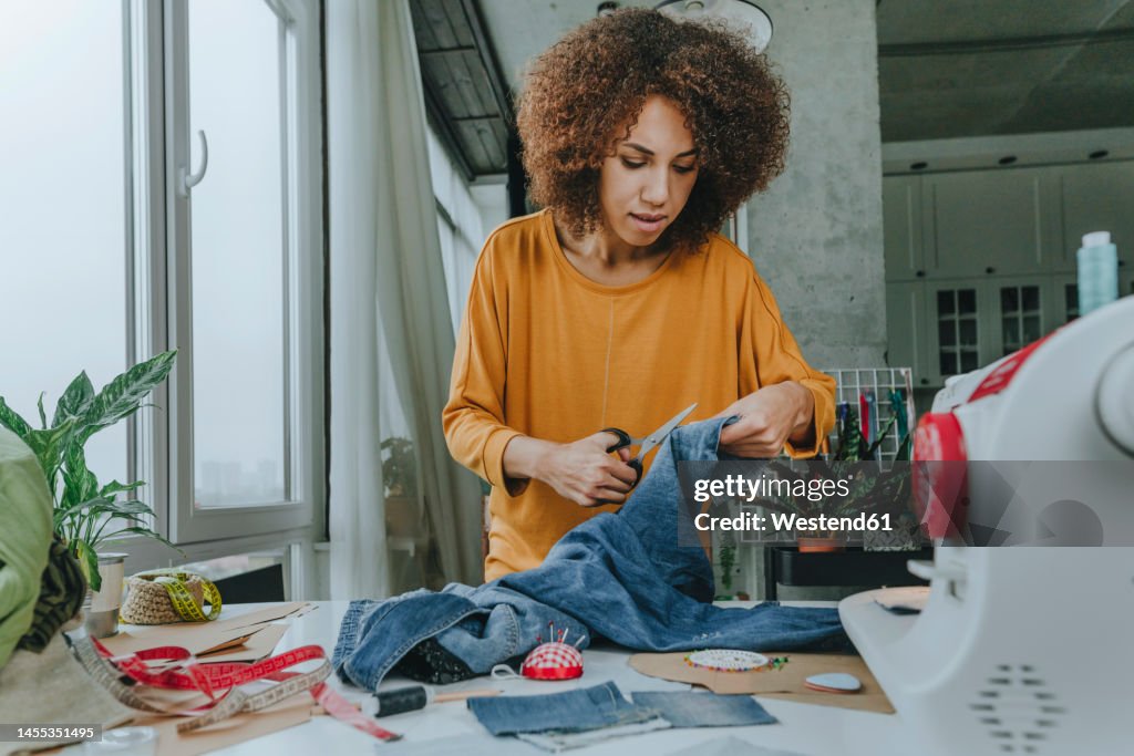 Fashion designer cutting jeans with scissors in workshop