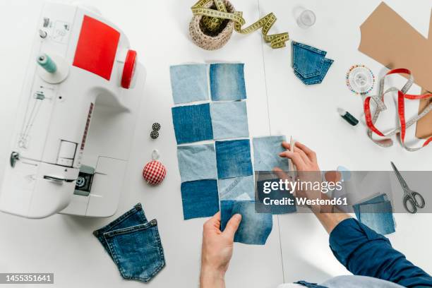 hands of fashion designer working on pieces of denim on table - patchwork stockfoto's en -beelden