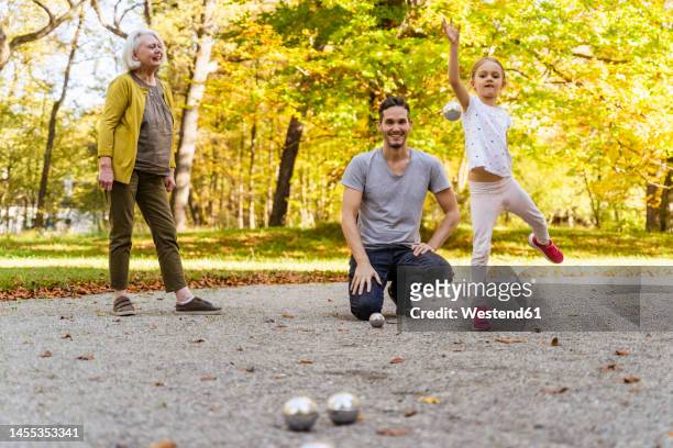 senior woman looking at girl playing boules with her father in park - 地擲球 個照片及圖片檔
