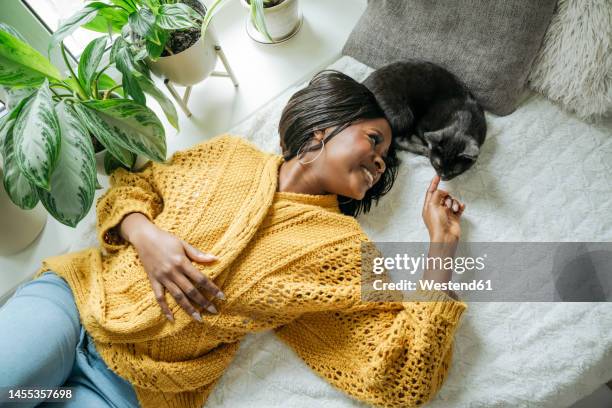 smiling young woman lying with cat at home - cat woman stock pictures, royalty-free photos & images