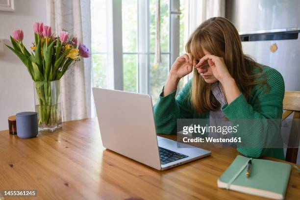 tired freelancer rubbing eyes sitting with laptop at table - rubbing eyes stock pictures, royalty-free photos & images