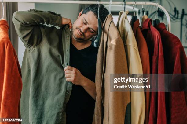 man putting on shirt standing by rack - getting dressed stock pictures, royalty-free photos & images