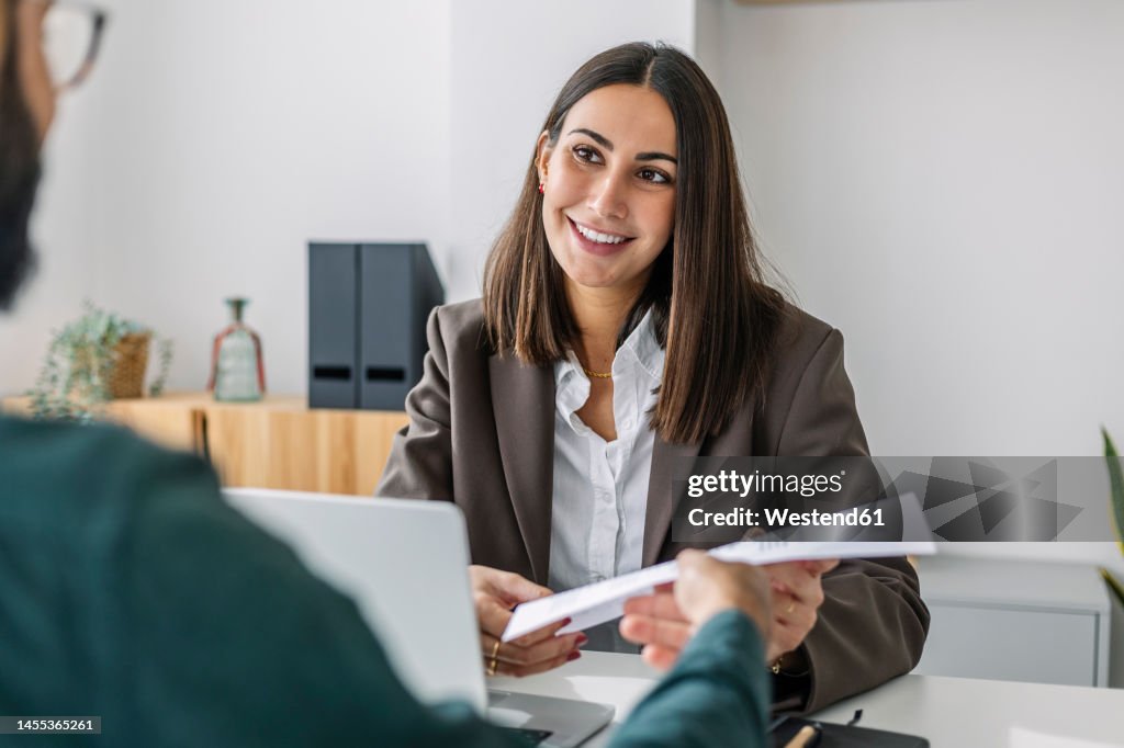 Candidate giving resume to recruiter at desk in workplace