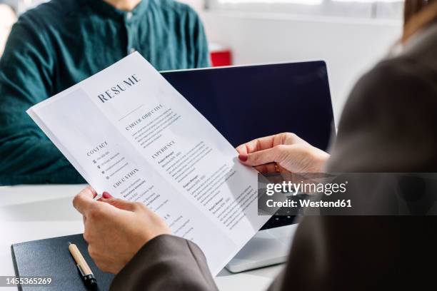 hands of recruiter holding resume in front of candidate at desk - currículum vitae fotografías e imágenes de stock