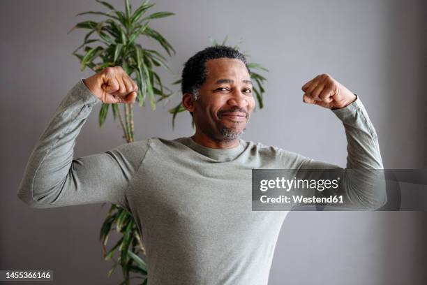 happy mature man flexing muscles in front of gray wall - flexionar los músculos fotografías e imágenes de stock
