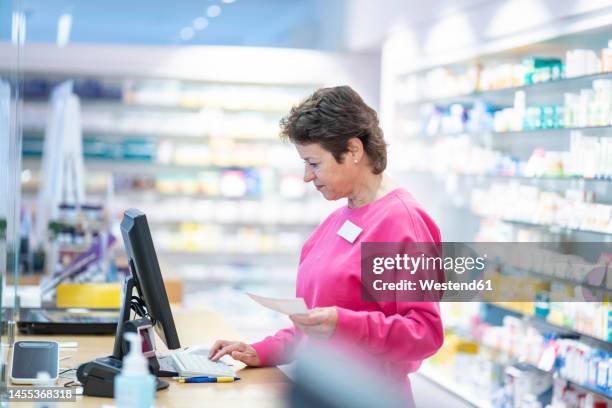 smiling pharmacist with medical prescription using computer at desk - apothekerin stock-fotos und bilder